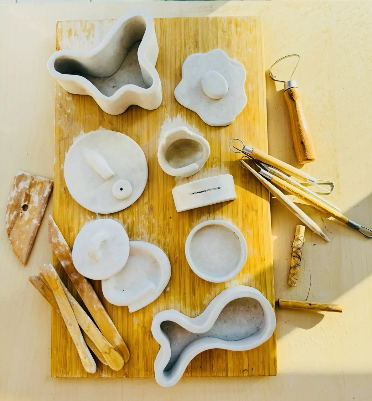 Handmade ceramic dishes and pottery tools on a wooden board